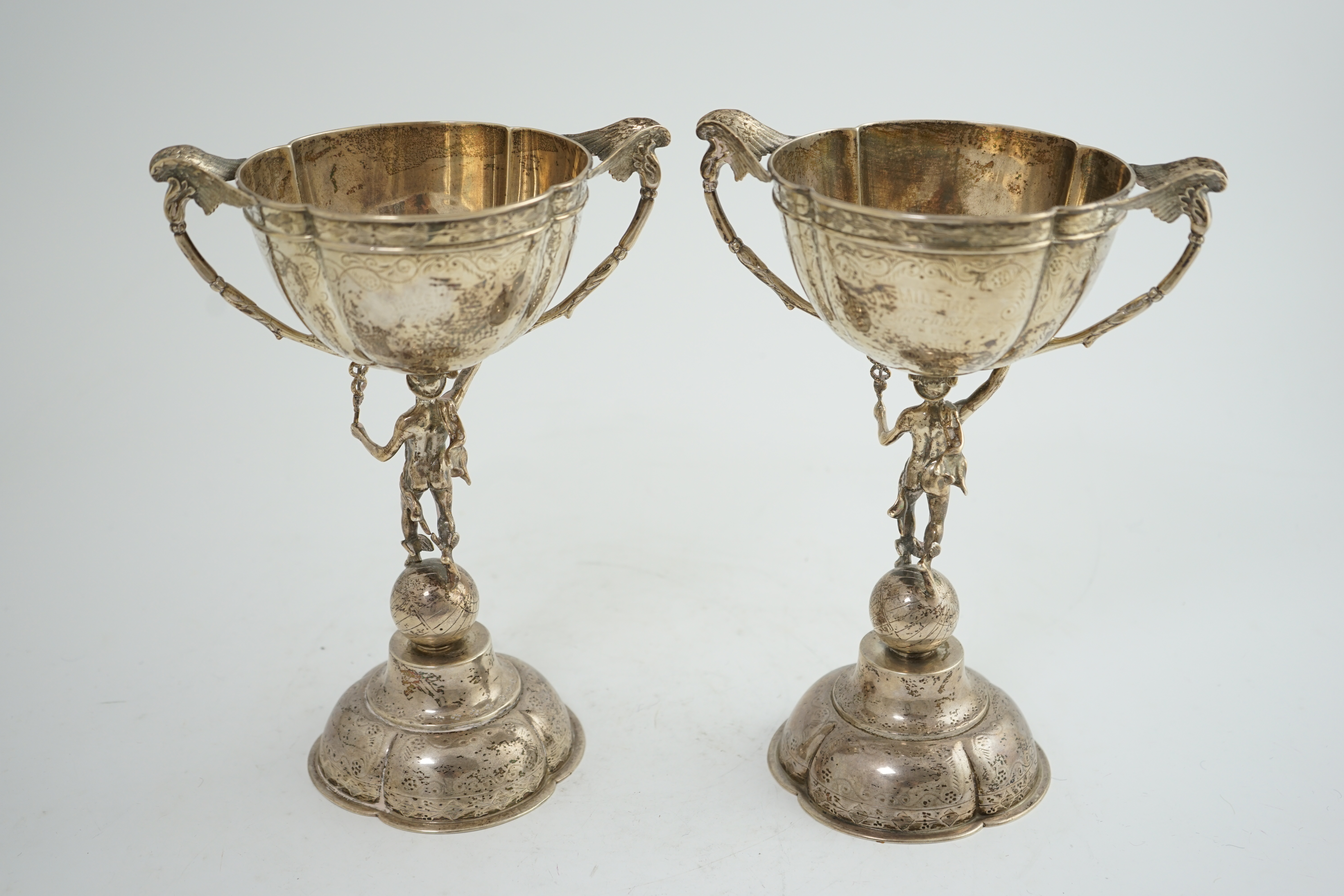 A pair of Victorian silver two handled pedestal cups, each figural stem modelled as Hermes upon a globe, by Edward Charles Brown